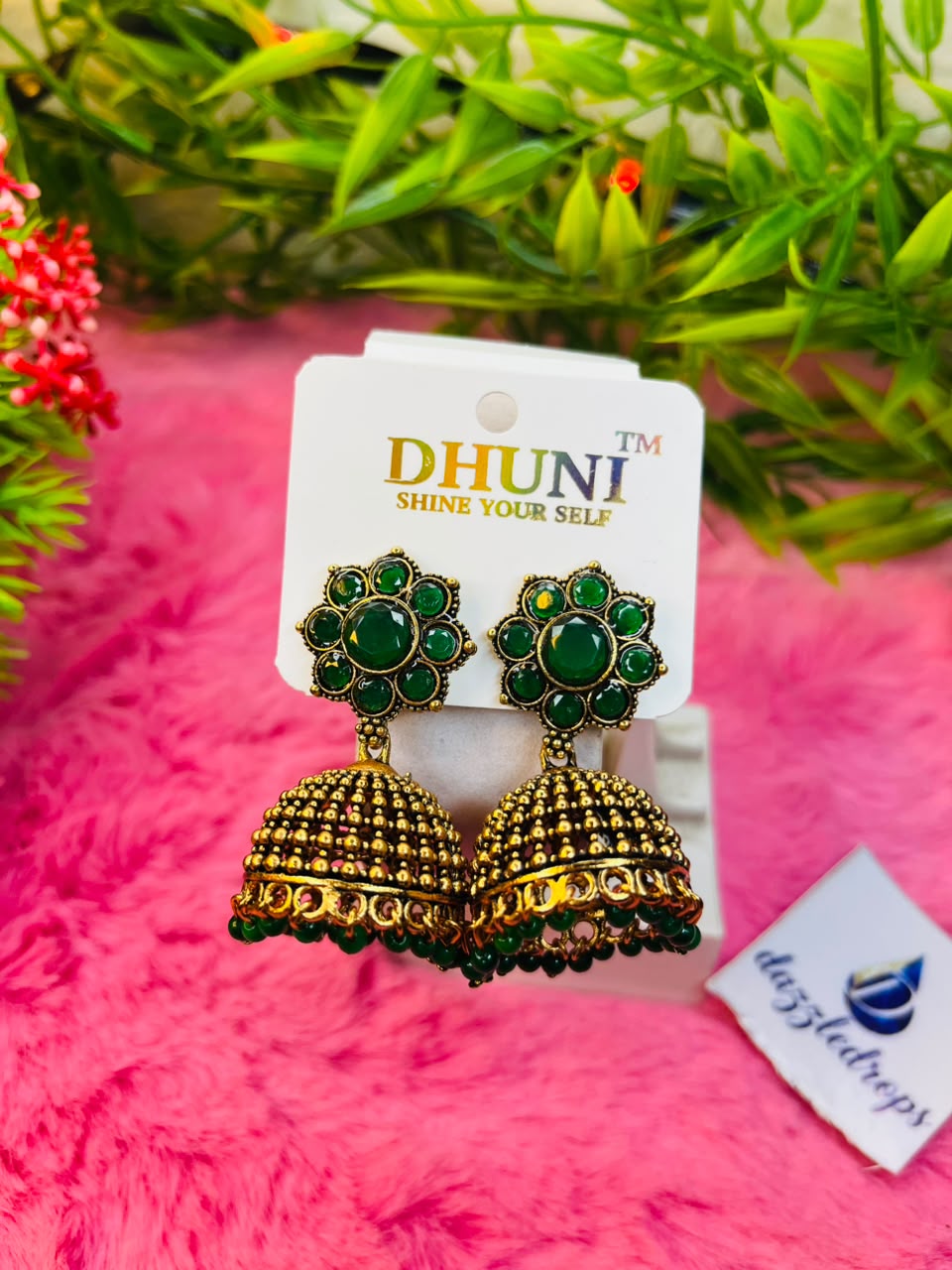 Antique gold floral jhumka earrings with stone studs and bead dangles on a pink plush background.