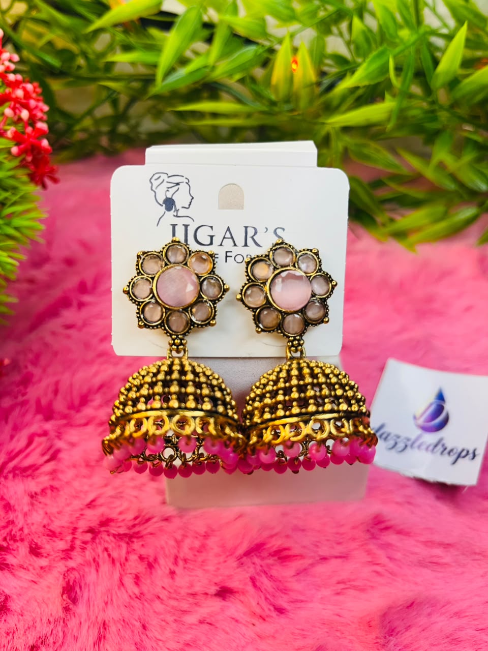 Antique gold floral jhumka earrings with stone studs and bead dangles on a pink plush background. — view 2